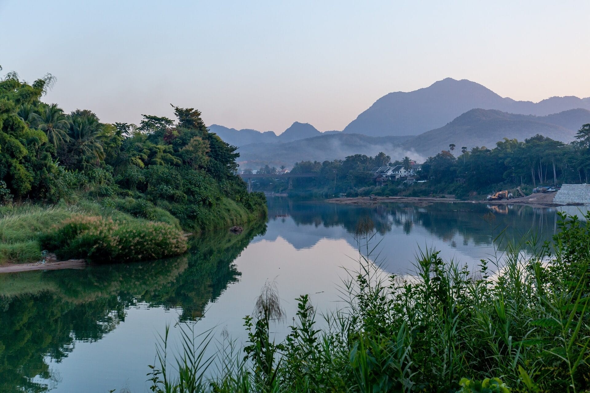 Scenic view of the Nam Khan River with lush greenery and mountains in the background in Luang Prabang, Laos.