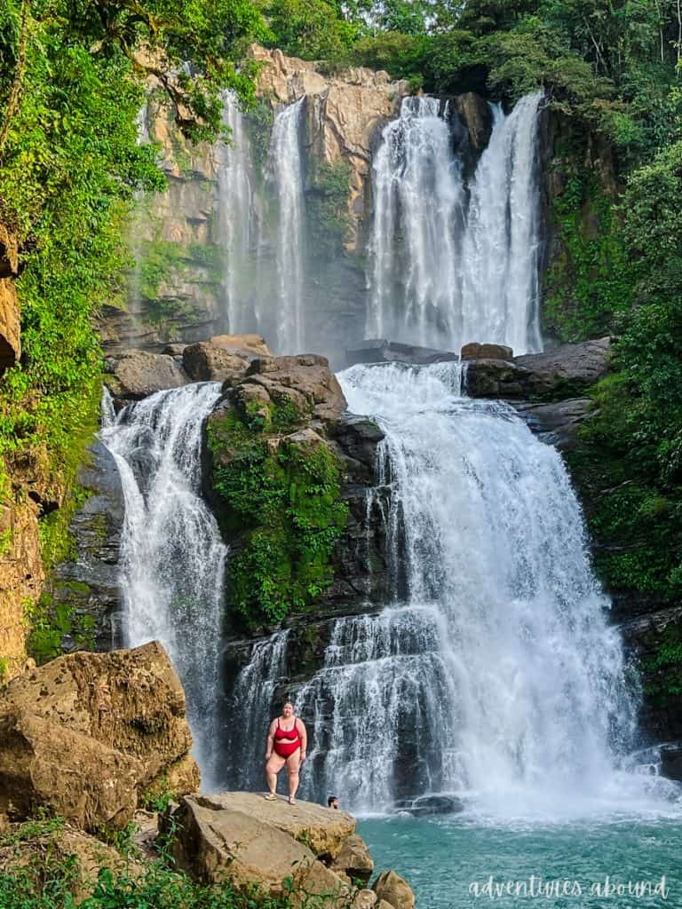 A woman in a red swimsuit poses on a rock in front of Nauyaca Waterfall, Costa Rica