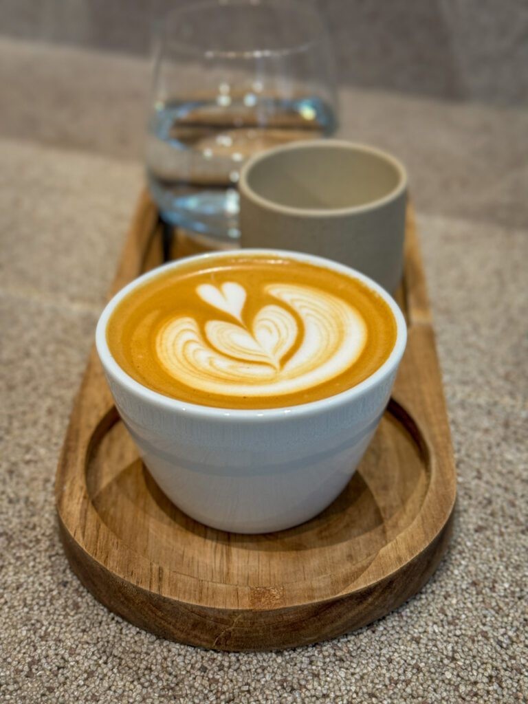 A close-up shot of a &quot;freeze distilled milk flat white&quot; at Nostos Coffee, showcasing its creamy texture and artful presentation