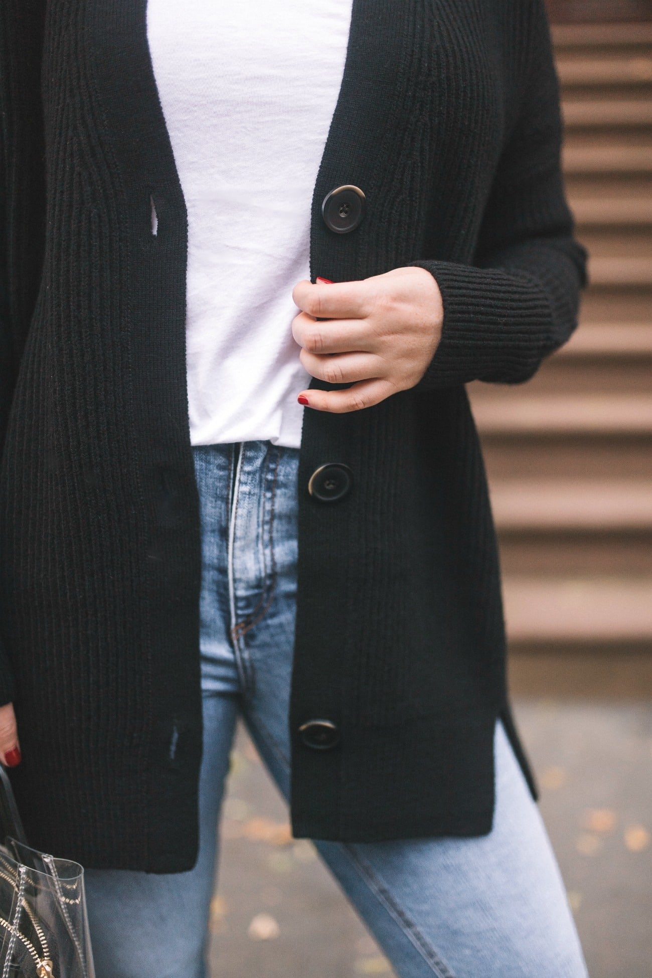 Close-up of a white, oversized cardigan hanging on a hanger, emphasizing its soft texture and loose fit, suggesting it as a comfortable layering piece for travel