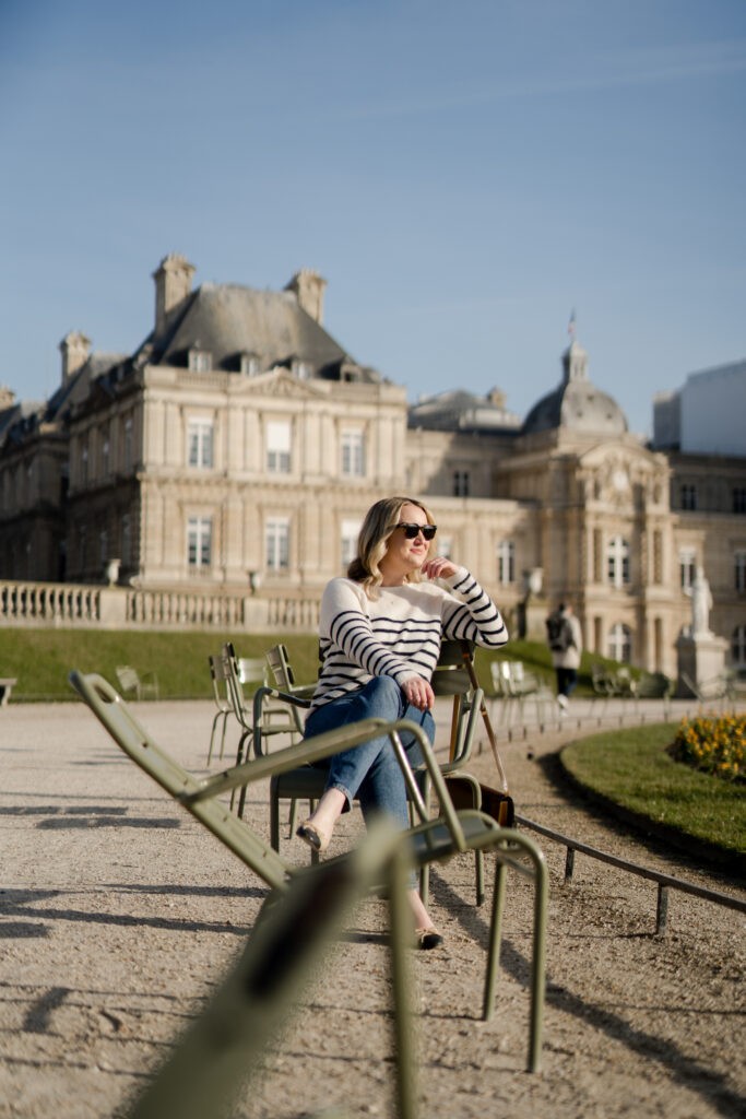 Woman enjoying shoulder season in a Paris park, wearing a stylish striped sweater