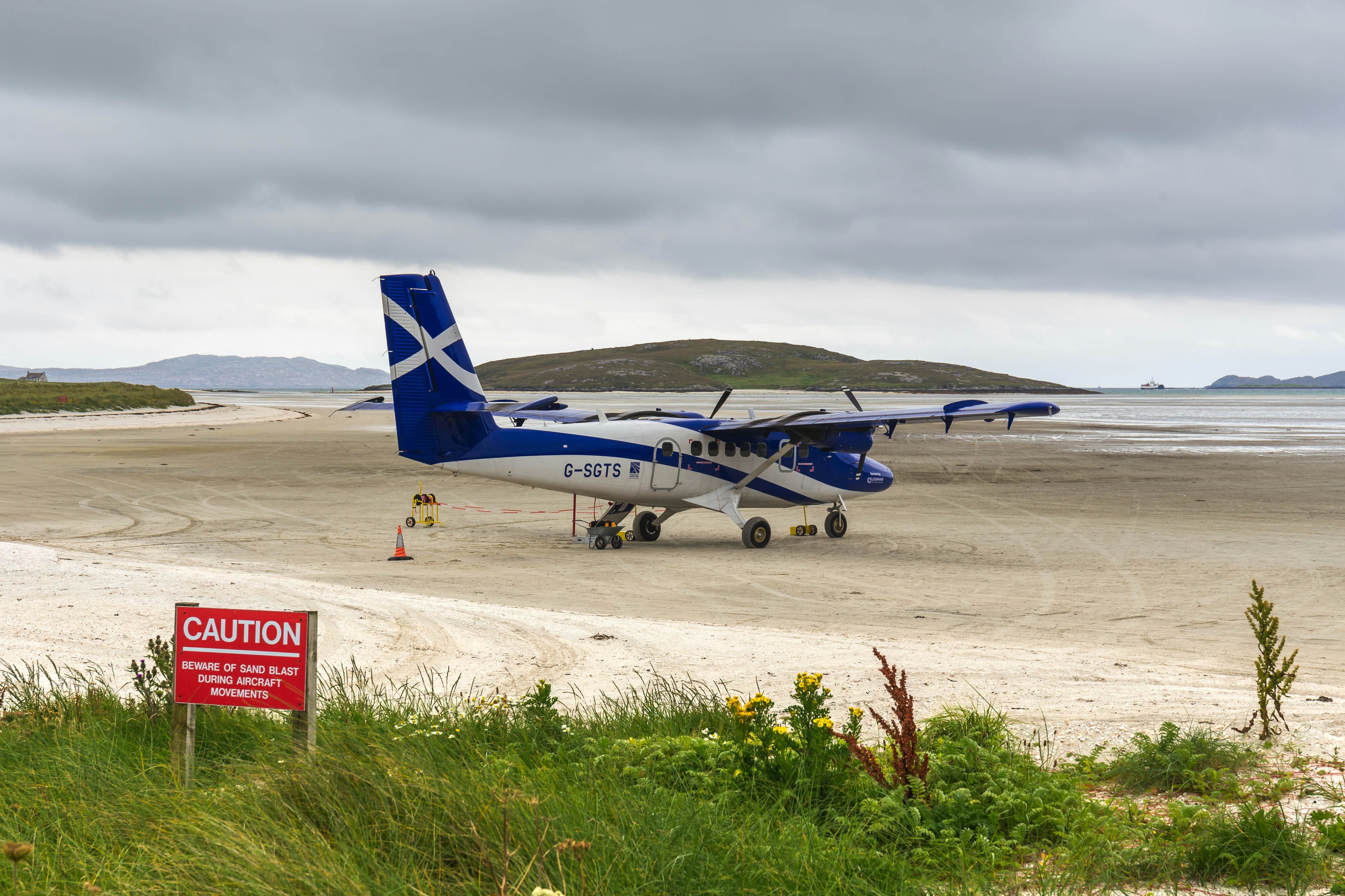 A small propeller plane painted in a blue and white livery on the sandy runway of Barra Airport, Barra, Outer Hebrides, Scotland