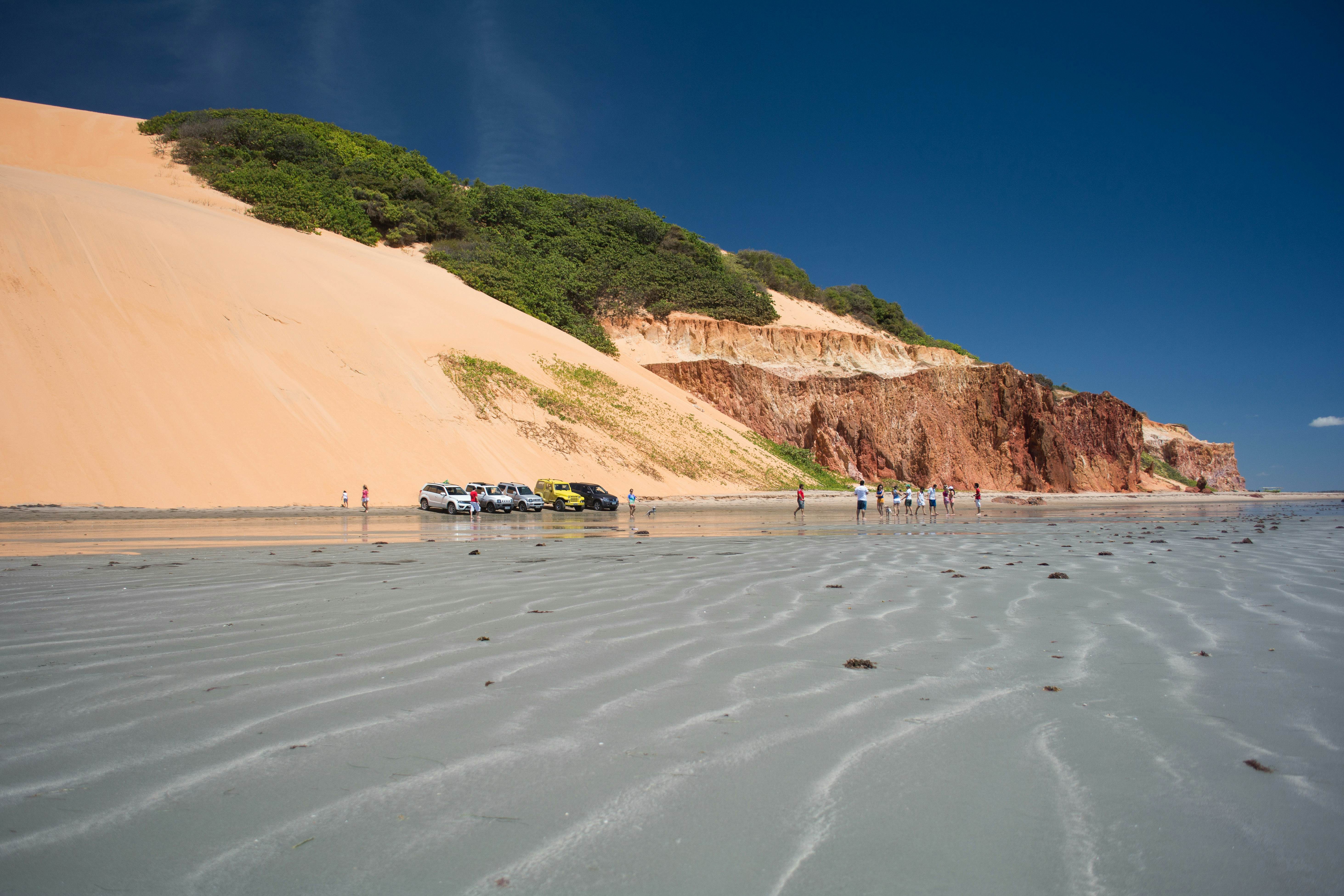 Tranquil beach scene with gentle waves, sand dunes, and distant cliffs, showcasing the serene beauty of Brazil's coast.