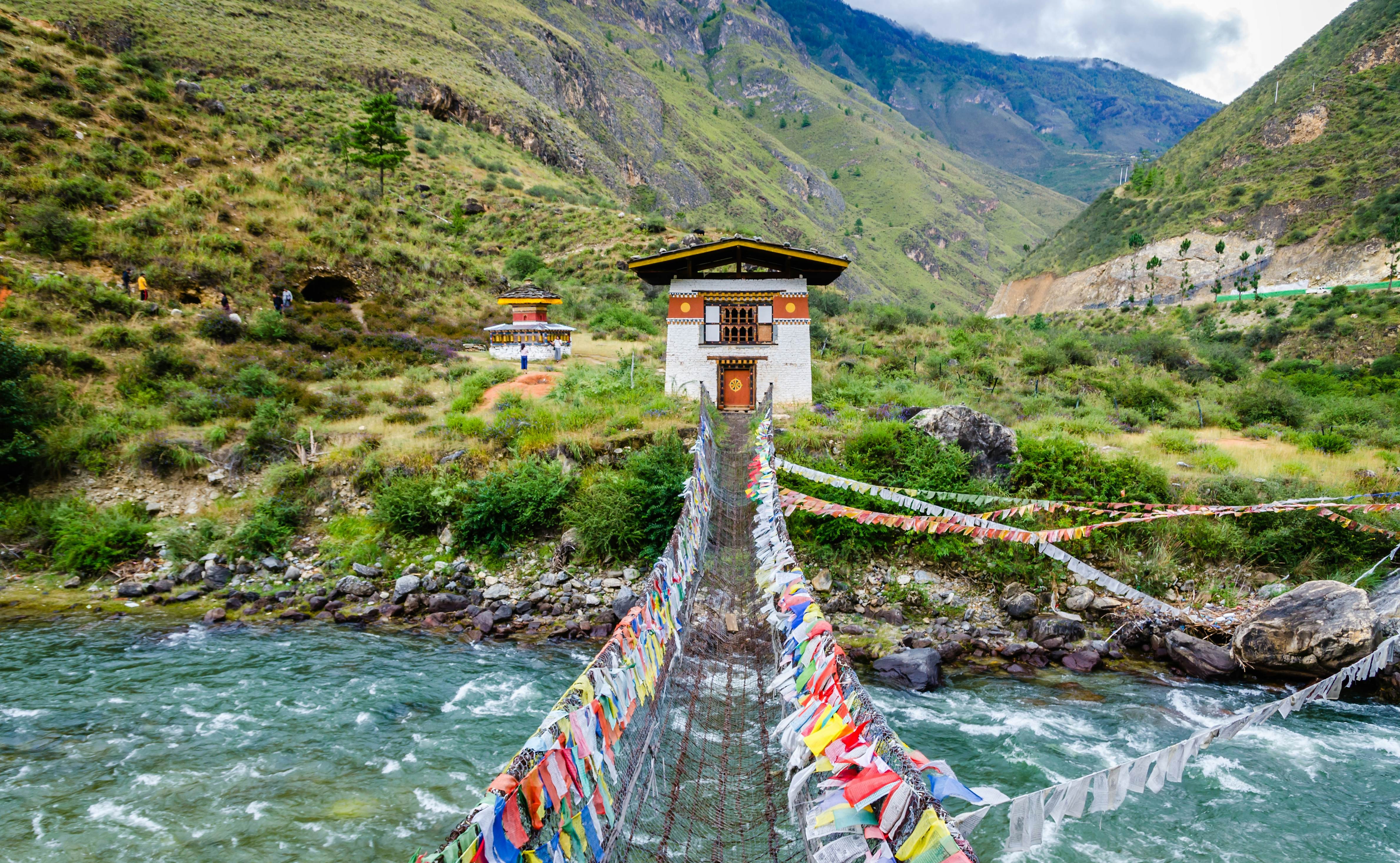 Paro, Bhutan, with a suspension bridge adorned with prayer flags, nestled in a mountainous valley under a clear sky