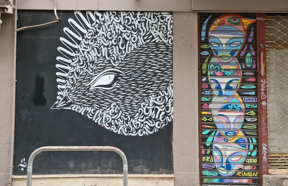 Street art: white on black, a figure of a fish composed of lots of symbols and letters. Beside it, on a shop