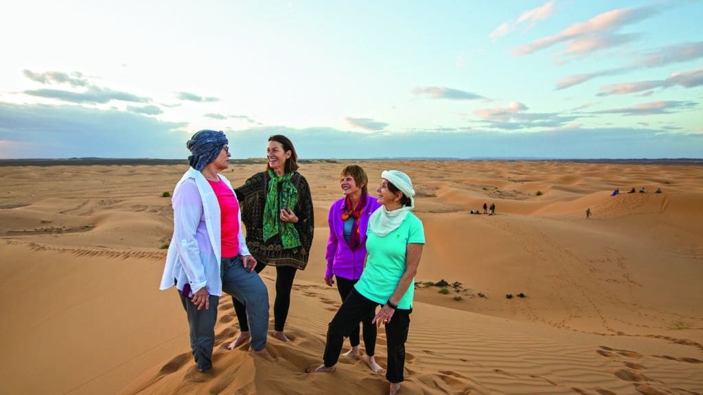 A group of people on an Overseas Adventure Travel tour stand on a sand dune