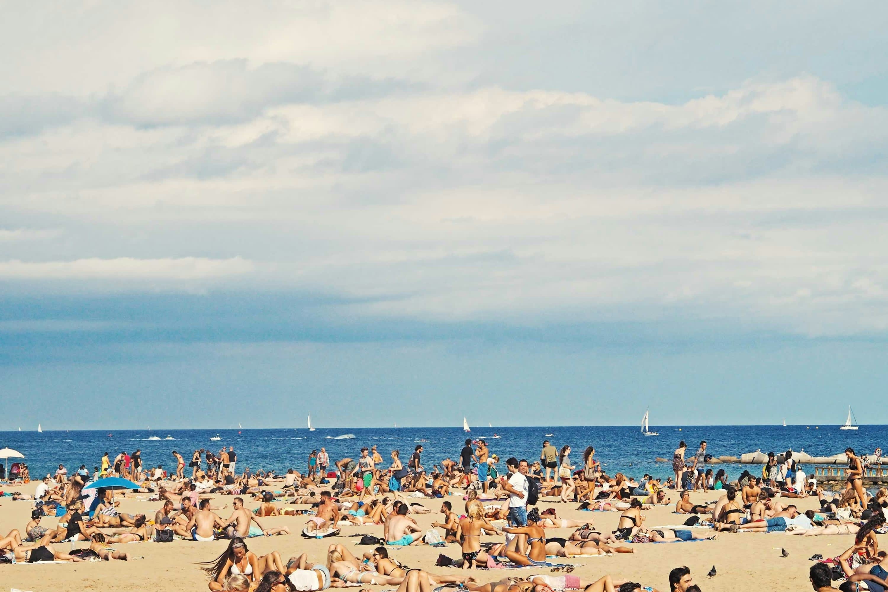 A beach crowded with locals and travelers on a partly cloudy day