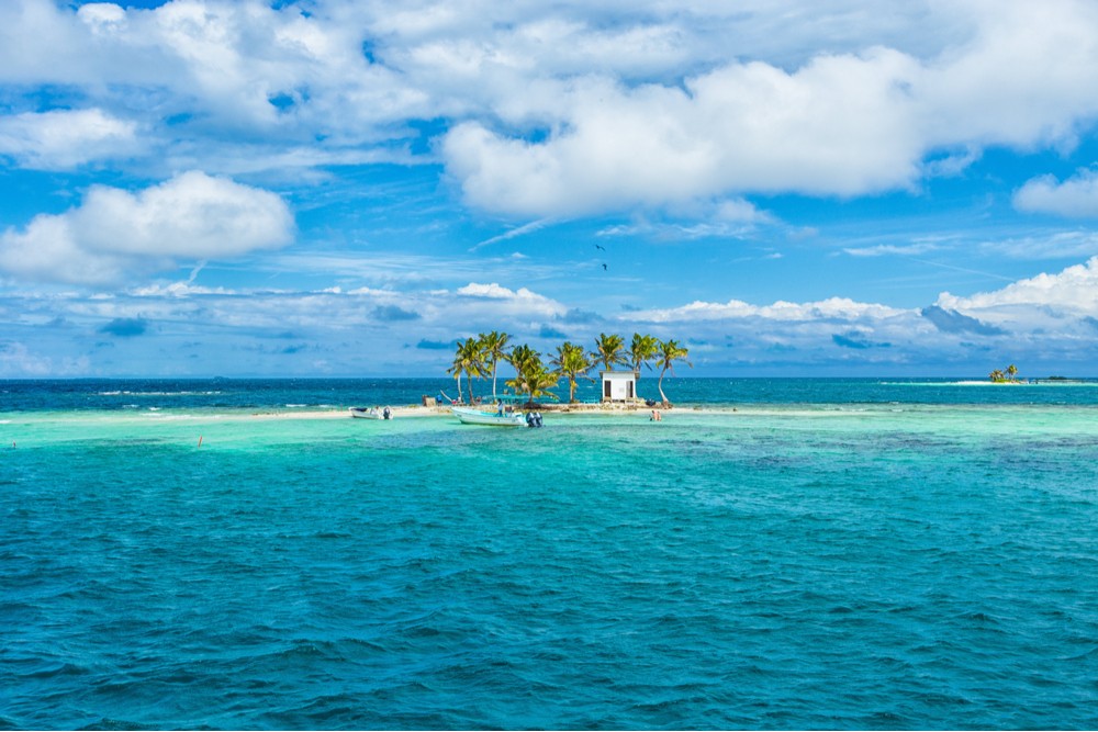 A picturesque tiny island in Belize, adorned with swaying coconut trees and surrounded by the vibrant turquoise waters of the Caribbean Sea, with a small boat gently floating nearby, capturing the essence of a secluded tropical paradise