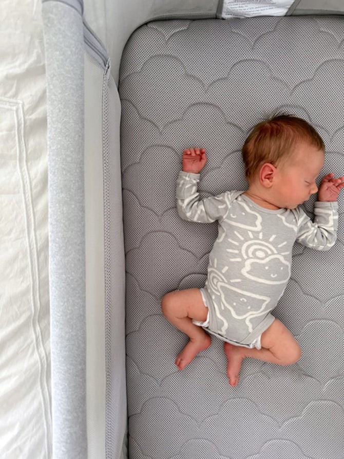 Baby peacefully sleeping on their back in a travel bassinet