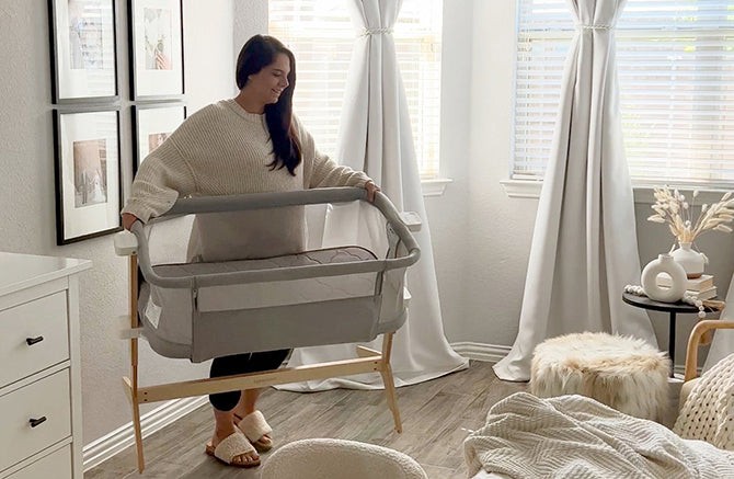 Mother carrying a folded travel bassinet over her shoulder while holding her baby