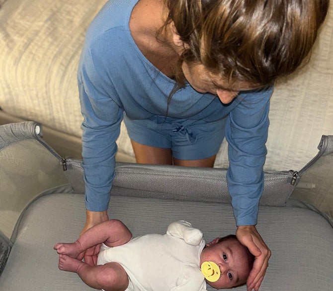 Woman gently placing newborn in a portable travel bassinet