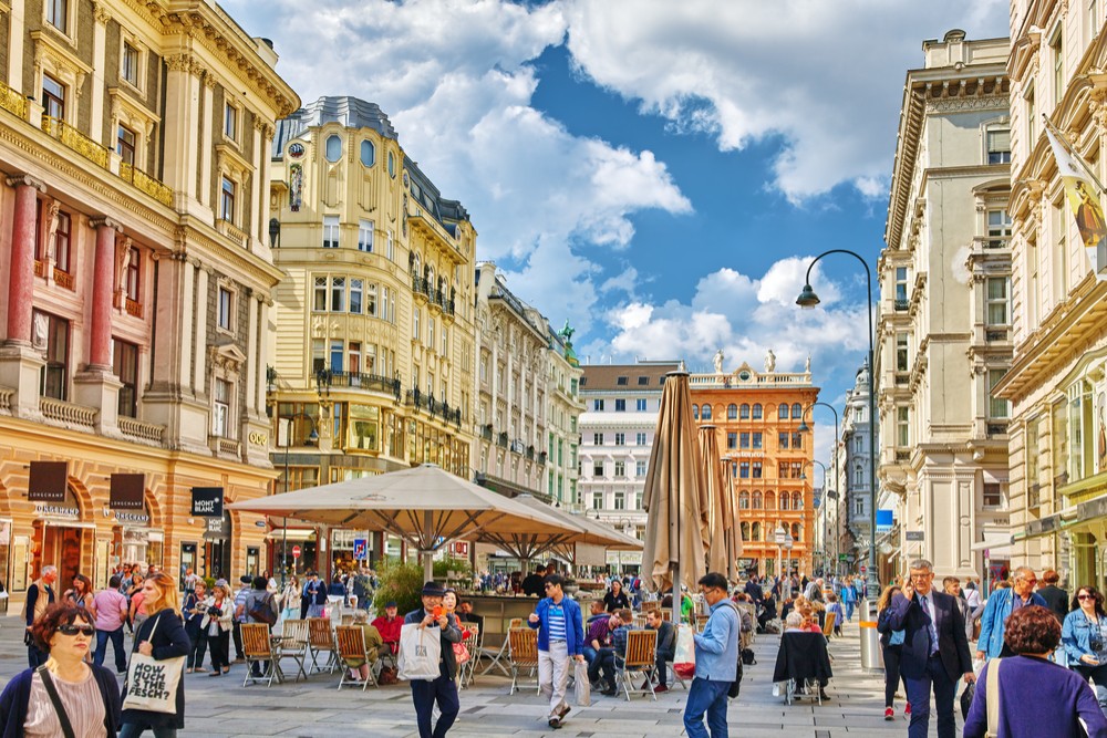 Cityscape views of Vienna, Austria, showcasing charming European architecture, bustling city streets with people, and a glimpse of spring foliage, capturing the vibrant atmosphere of a Central European city in April