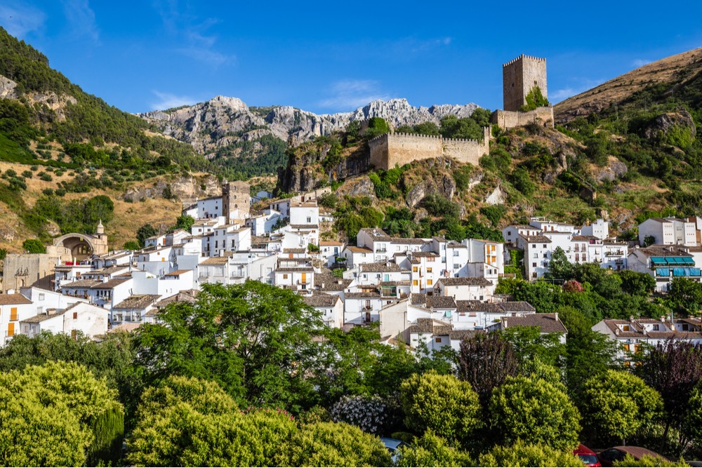 The historic City of Cazorla and Yedra Castle in Andalusia, Spain, perched on a hilltop overlooking whitewashed buildings and rolling hills, bathed in warm sunlight, showcasing the region's rich cultural heritage and scenic beauty