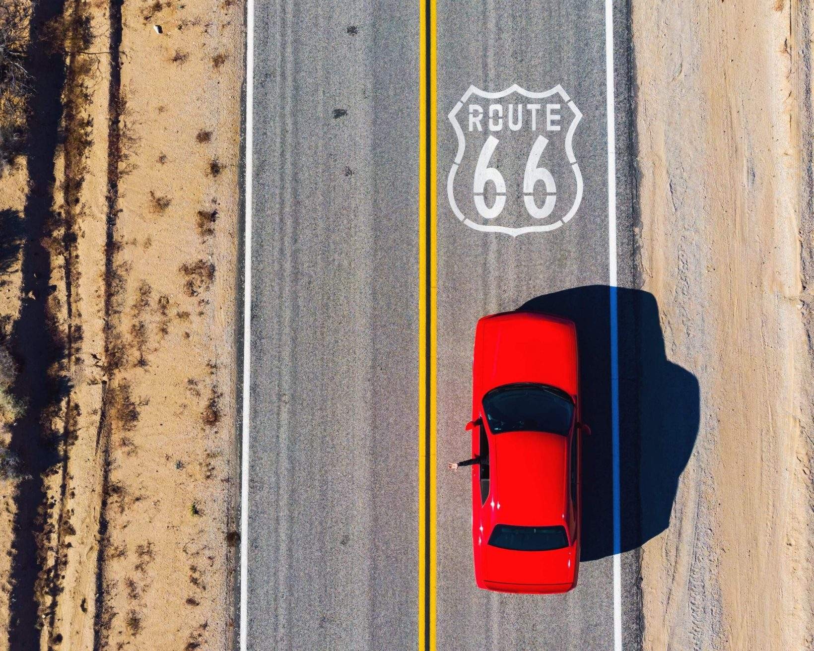 A red car driving down the Route 66 highway.
