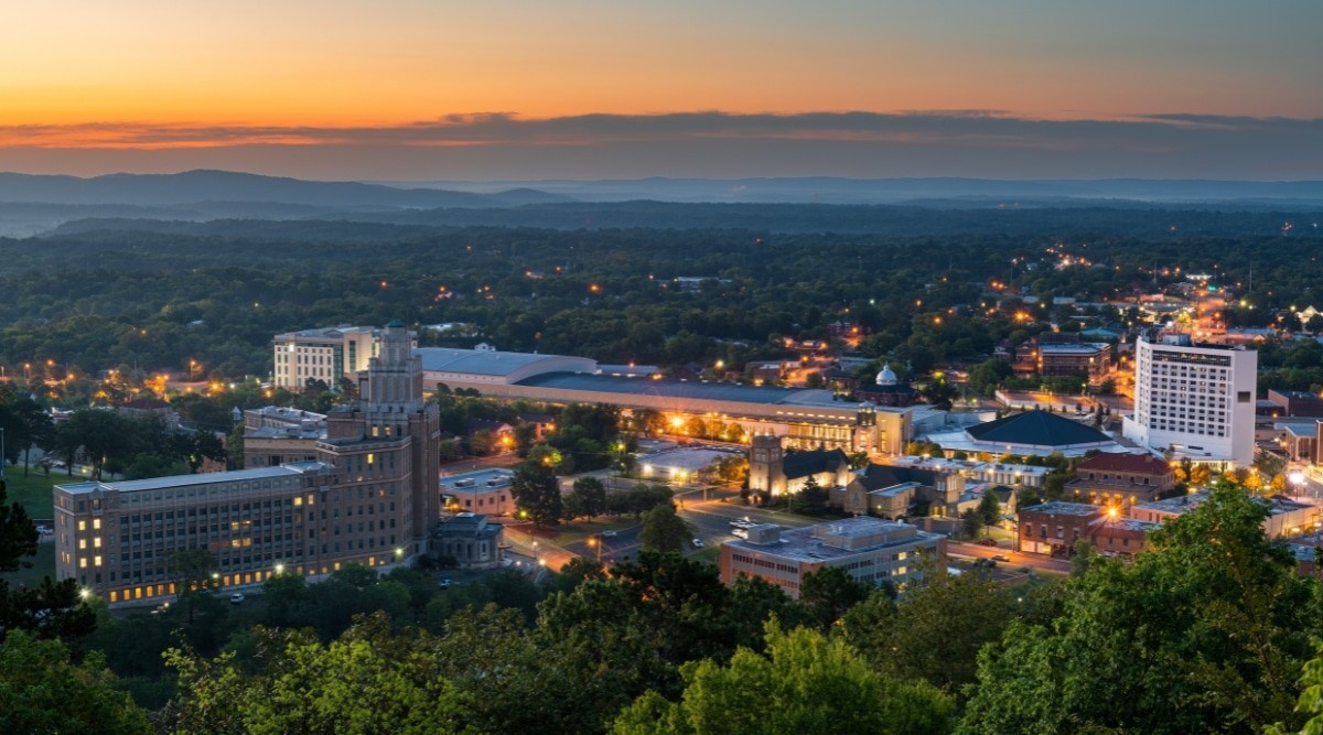 An evening view of Hot Springs, Arkansas, illuminated with yellow lights and surrounded by greenery.