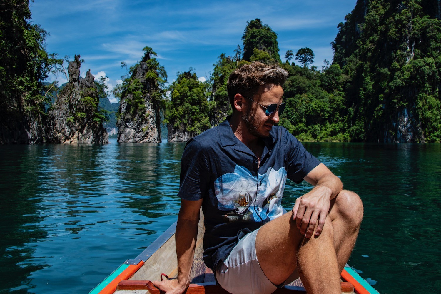 Khao Sok National Park, featuring a serene lake surrounded by lush greenery and limestone cliffs, suggesting a tranquil escape during the potentially hot and humid month of May.