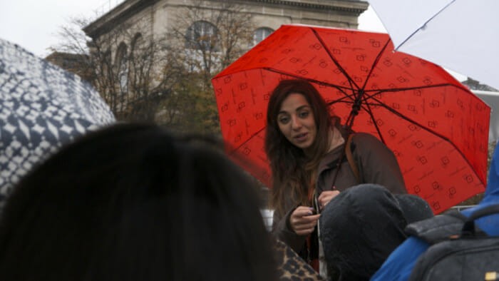 A smiling tour guide leads a group of tourists on a wet, cobblestone street in Paris