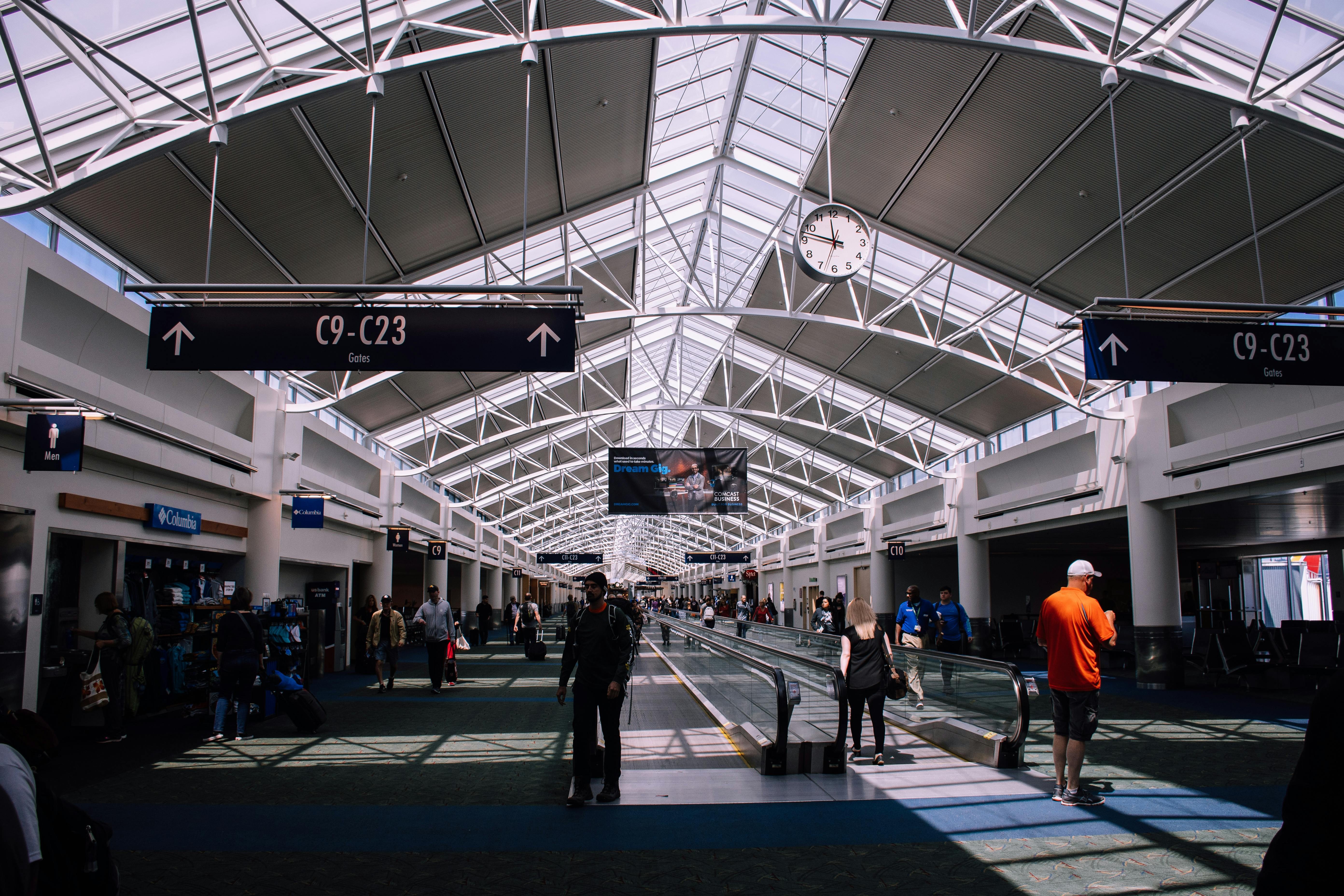 Exterior view of a modern airport terminal with glass windows, passenger walkways, and airline logos.