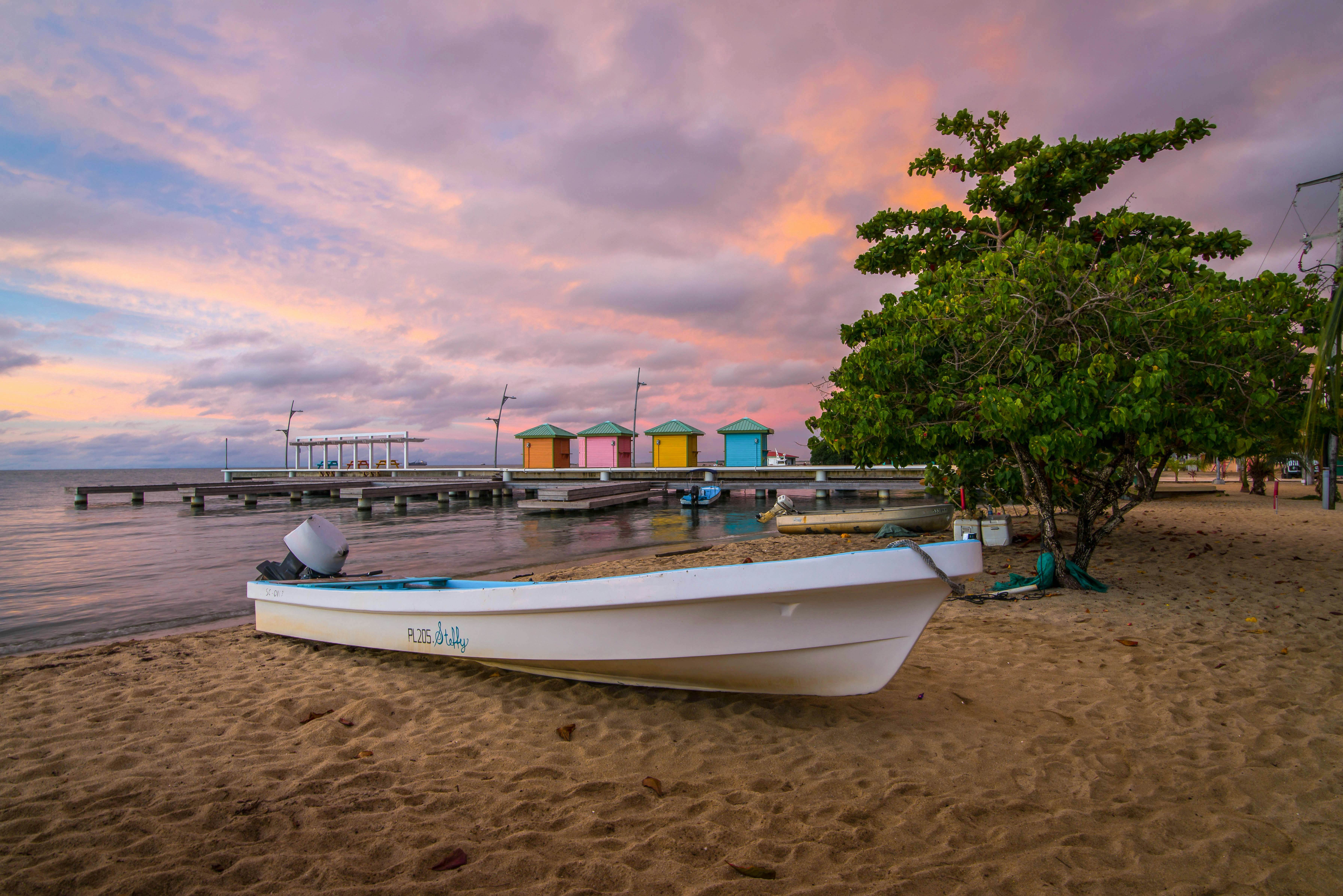 Wooden boat docked on a sandy beach, with lush palm trees and clear blue water in the background, representing the tranquil coastal scenery of Punta Gorda, Belize