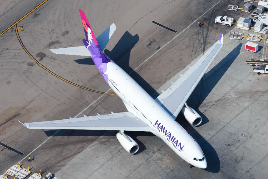Hawaiian Airlines airplane soaring above tropical islands, symbolizing the airline's unique travel benefits.