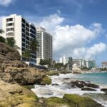 Waves crashing on rocks with buildings in the background