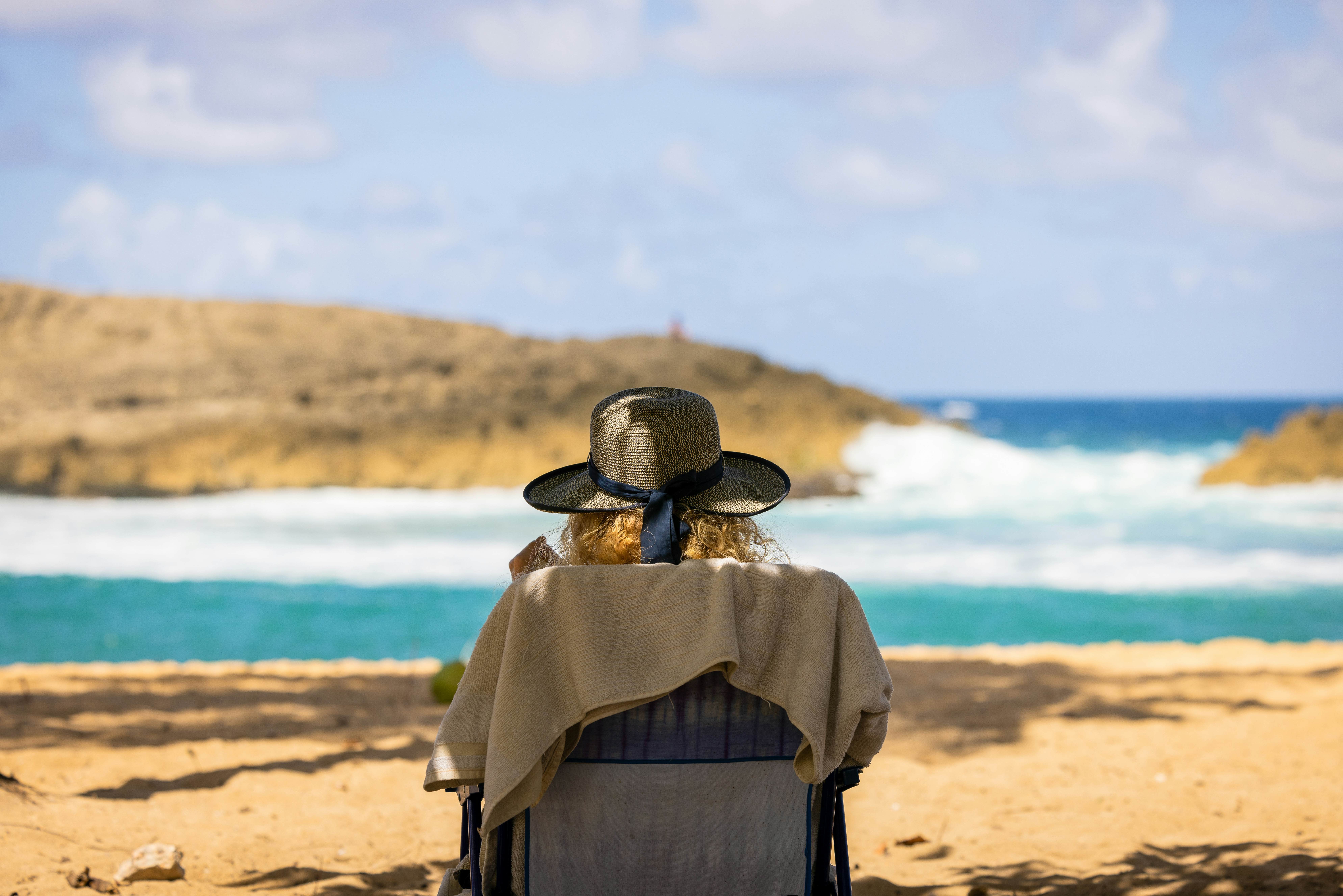 A woman sitting on the beach wearing a sun hat