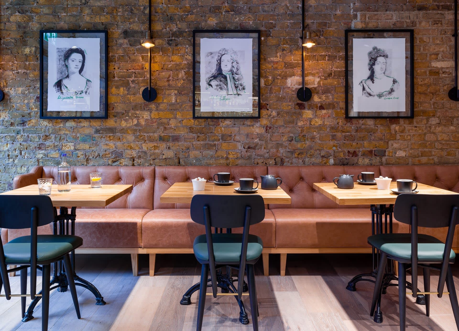 An orange booth and teal chairs in front of a brick wall in a chic restaurant
