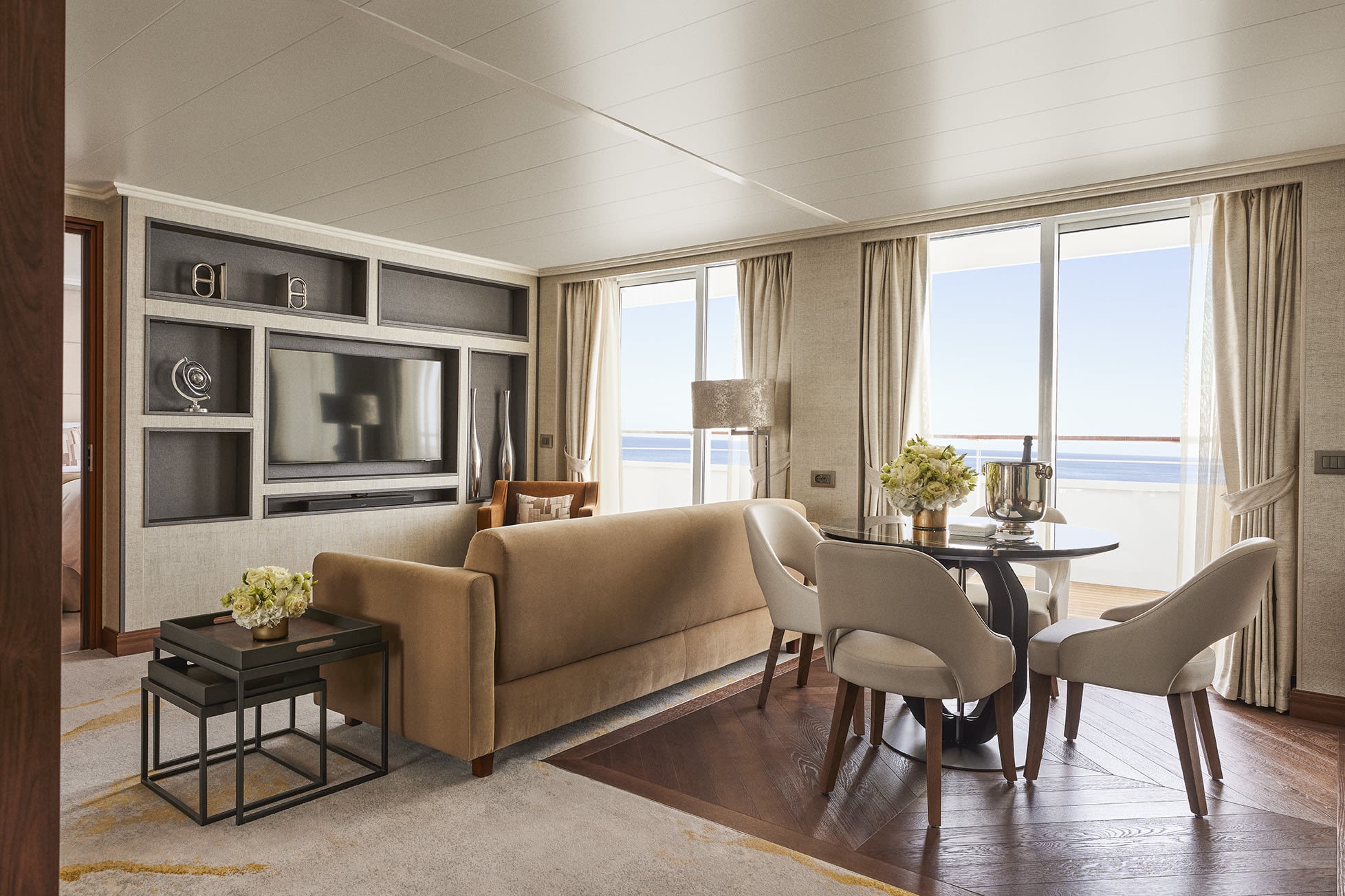 A luxe cruise living room with wooden floors and a balcony overlooking the ocean, illustrating the potential for luxurious travel experiences in the travel industry