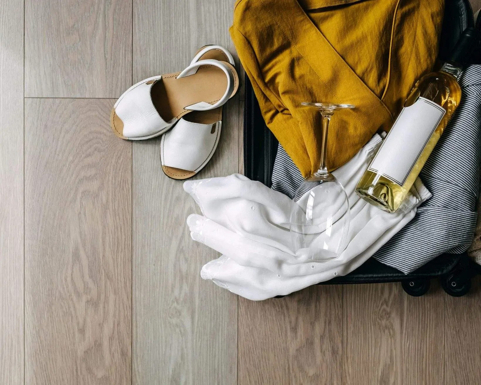 Suitcase containing clothes, wine, and sandals, illustrating vacation packing