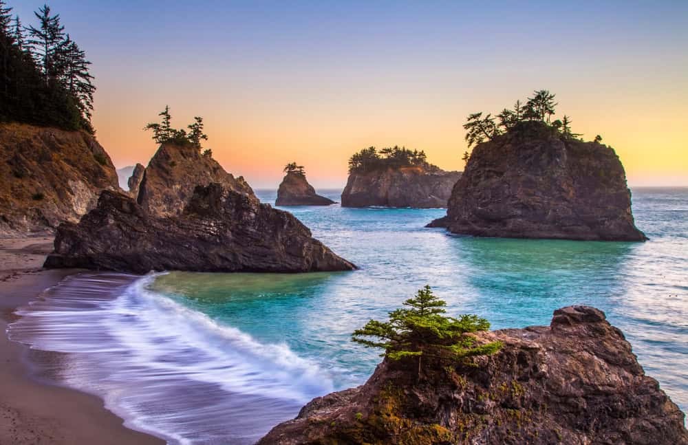 Haystack Rock at Cannon Beach shows the iconic landmark surrounded by the ocean and sandy beach.