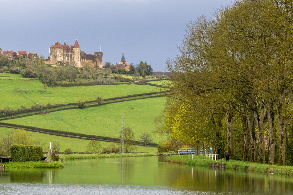 Chateauneuf-en-Auxois Castle with canal in Burgundy, France. A canal winds past the castle.