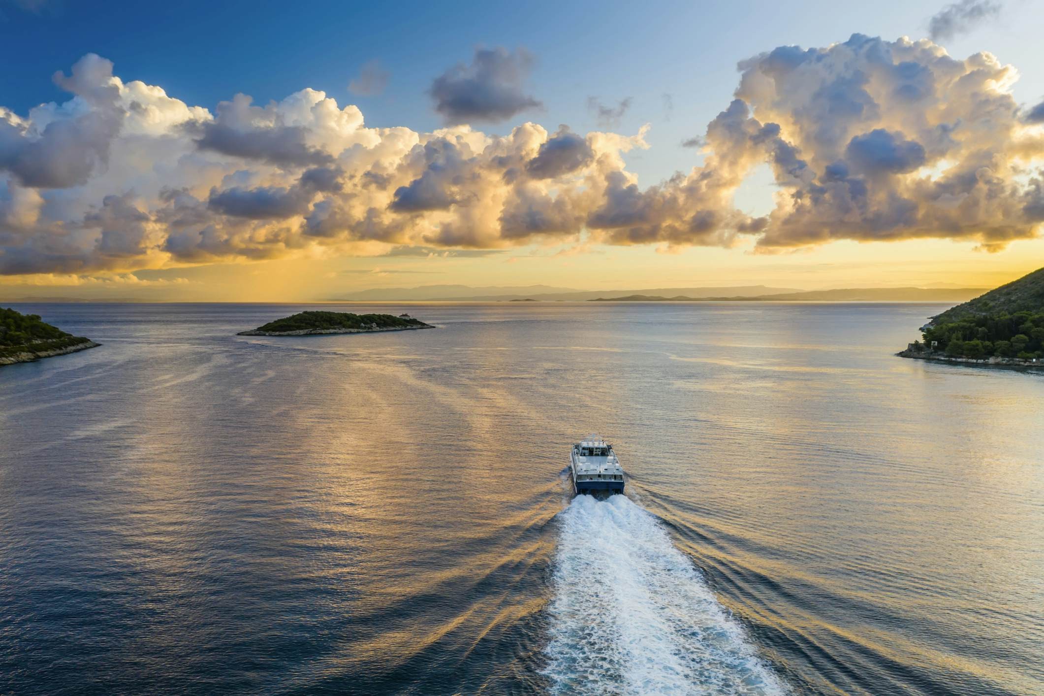 Ferry sailing across the sea with islands and sunset in the background
