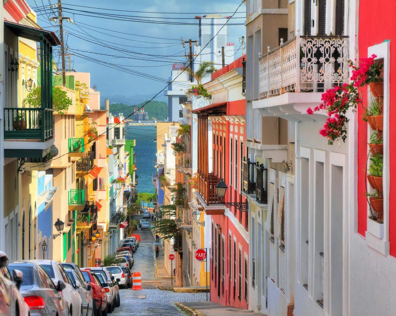 A narrow street with parked vehicles on one side flanked by colourful buildings, showcasing the vibrant streets of Old San Juan