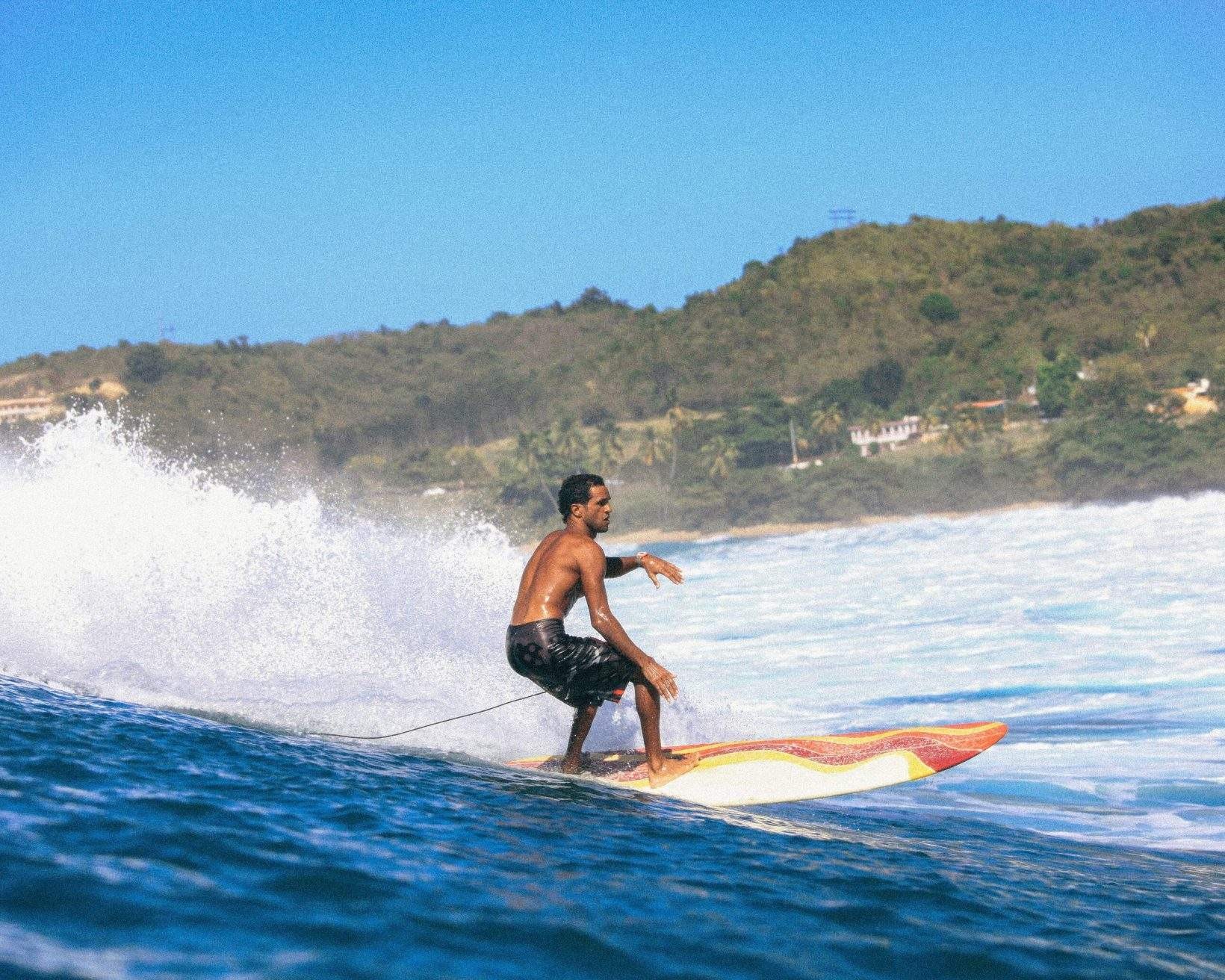 A man skillfully surfs on the wavy beach by the lush island, showcasing the surfing opportunities in Puerto Rico