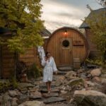 Woman walking across large stones in front of a barrel-shaped wooden building in Quebec
