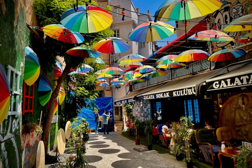 Rainbow umbrellas hover over a street of shops and restaurants in Istanbul Turkey. Enjoy a crowd-free stroll through Istanbul.