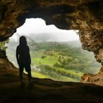 Silhouette of a person looking at a green valley from a cave