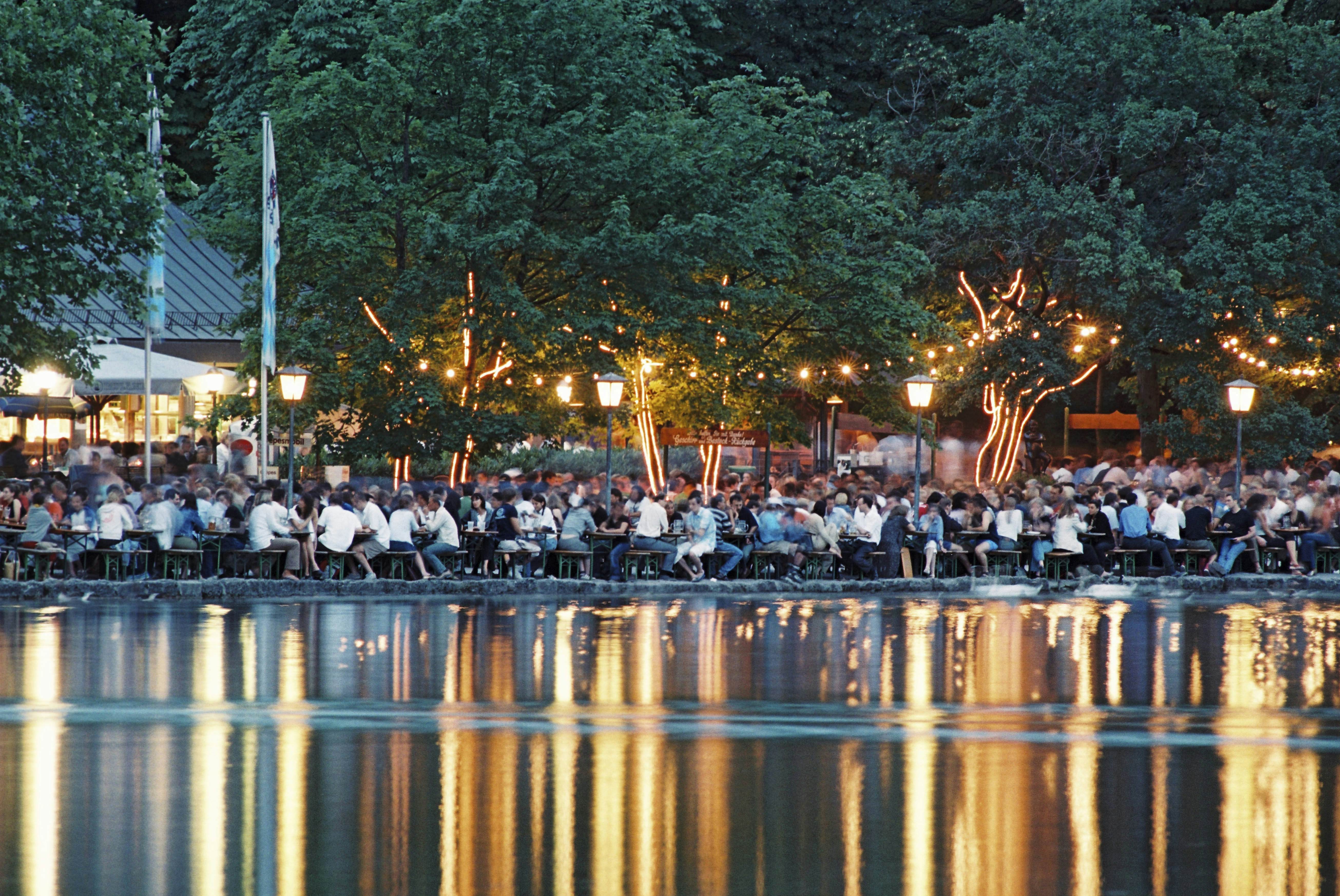 People crowd outdoor tables at the beer garden of Seehaus and reflected in the water