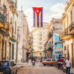 The red, white, and blue flag of Cuba hangs down between buildings in a street in Old Havana
