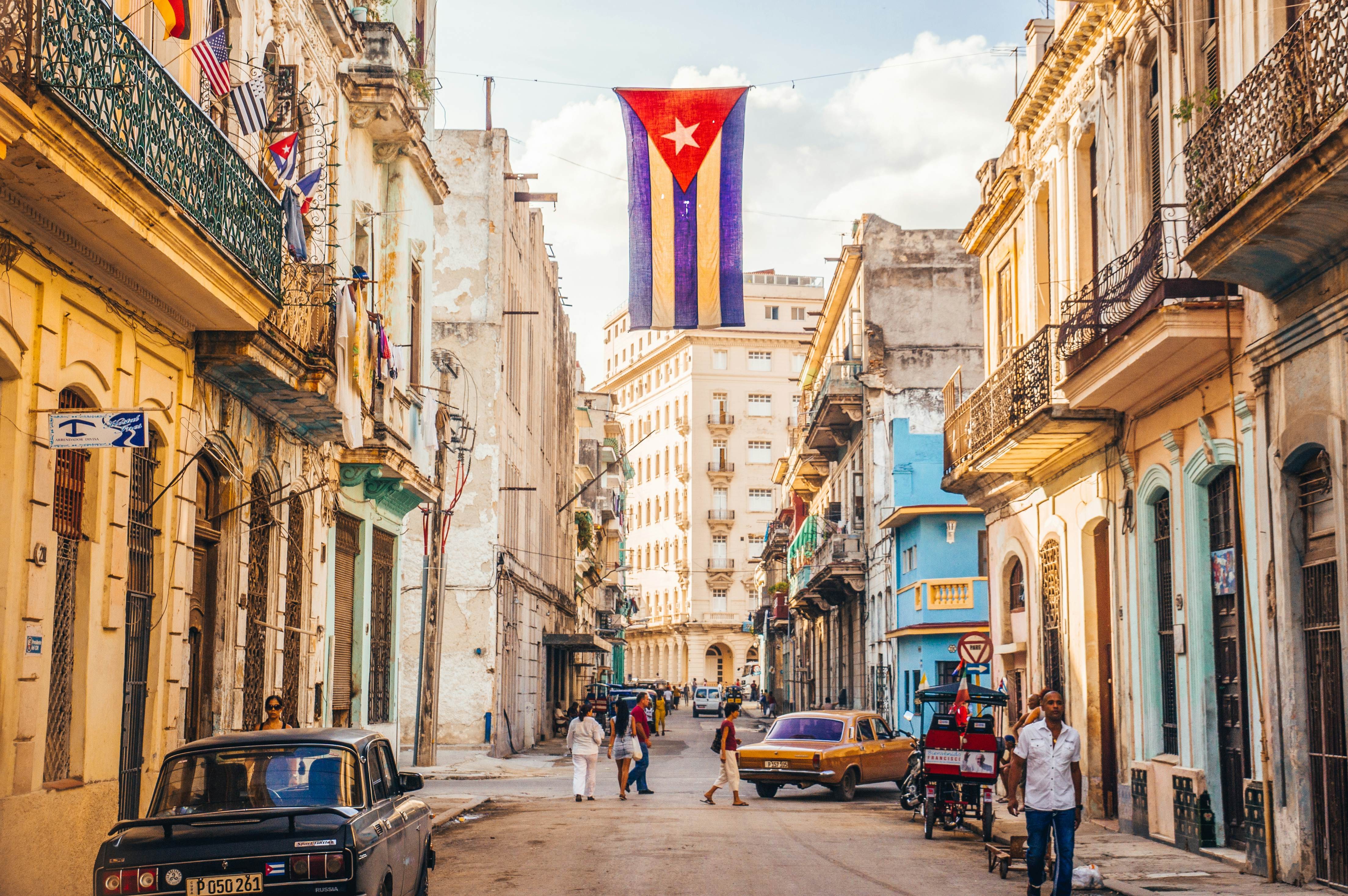The red, white, and blue flag of Cuba hangs down between buildings in a street in Old Havana