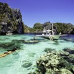 A woman snorkels in clear water next to a boat with pontoons in a rocky lagoon