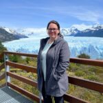 Perito Moreno Glacier towering majestically, reflecting in the turquoise water, surrounded by snow-capped mountains and clear blue skies, capturing the grandeur and serene beauty of Los Glaciares National Park.