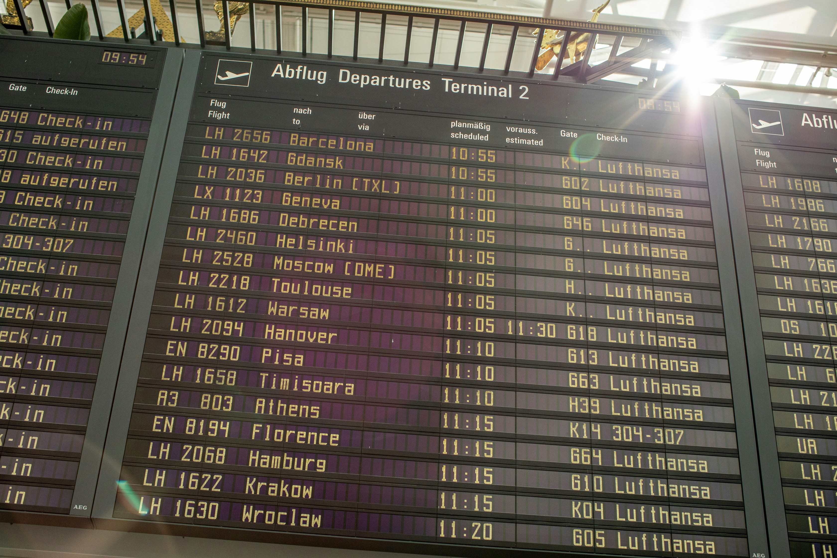 A terminal departure board displays upcoming Lufthansa flights to various European cities, detailing flight numbers and times.