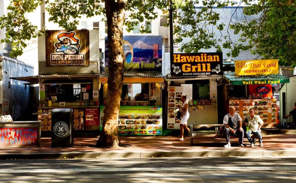 Portland food cart pods are busy with people showing a variety of culinary options and outdoor seating.