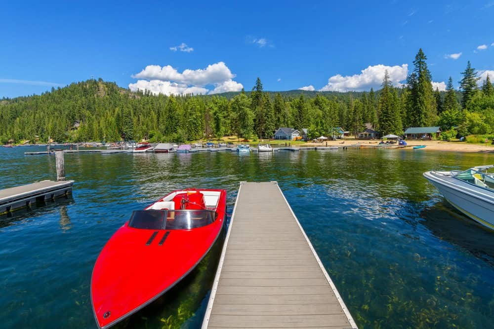 Boats dot Priest Lake showing the clear waters and surrounding evergreen forests under a sunny sky.