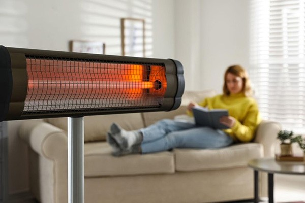 Woman reading book in living room with electric infrared heater, illustrating the conversion of electrical energy to radiant heat.