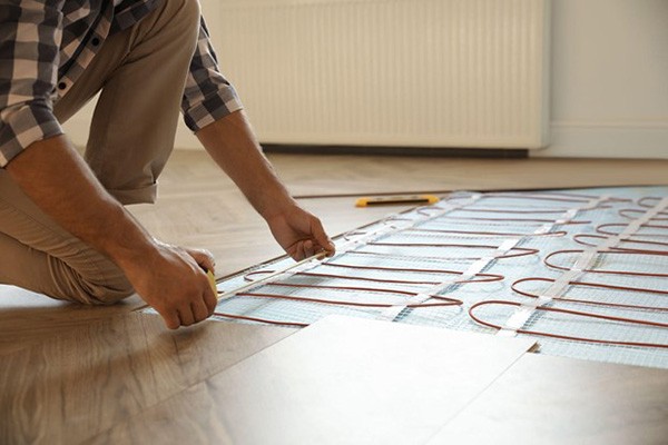Professional worker installing electric underfloor heating system indoors, illustrating radiant heating technology.