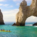 Kayakers paddling near the iconic stone arch of Cabo San Lucas under a sunny sky