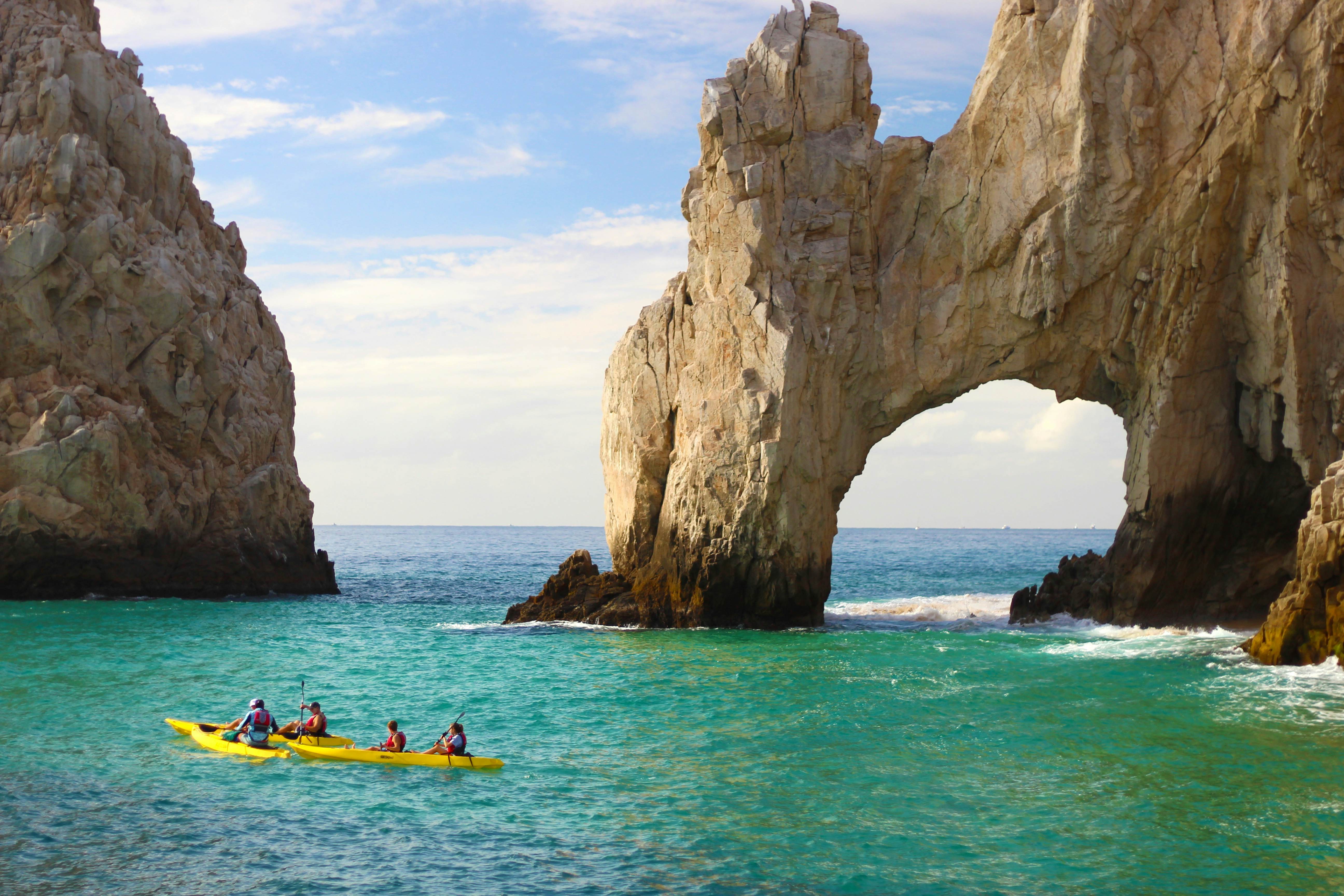 Kayakers paddling near the iconic stone arch of Cabo San Lucas under a sunny sky