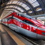 A Frecciarossa 1000 train speeds through the Italian countryside, showcasing its sleek design